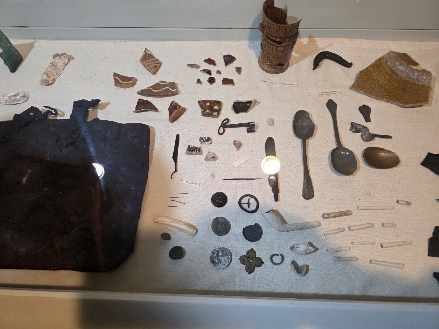 Archaeological display with pottery, utensils, pipe stems, and iron fragments