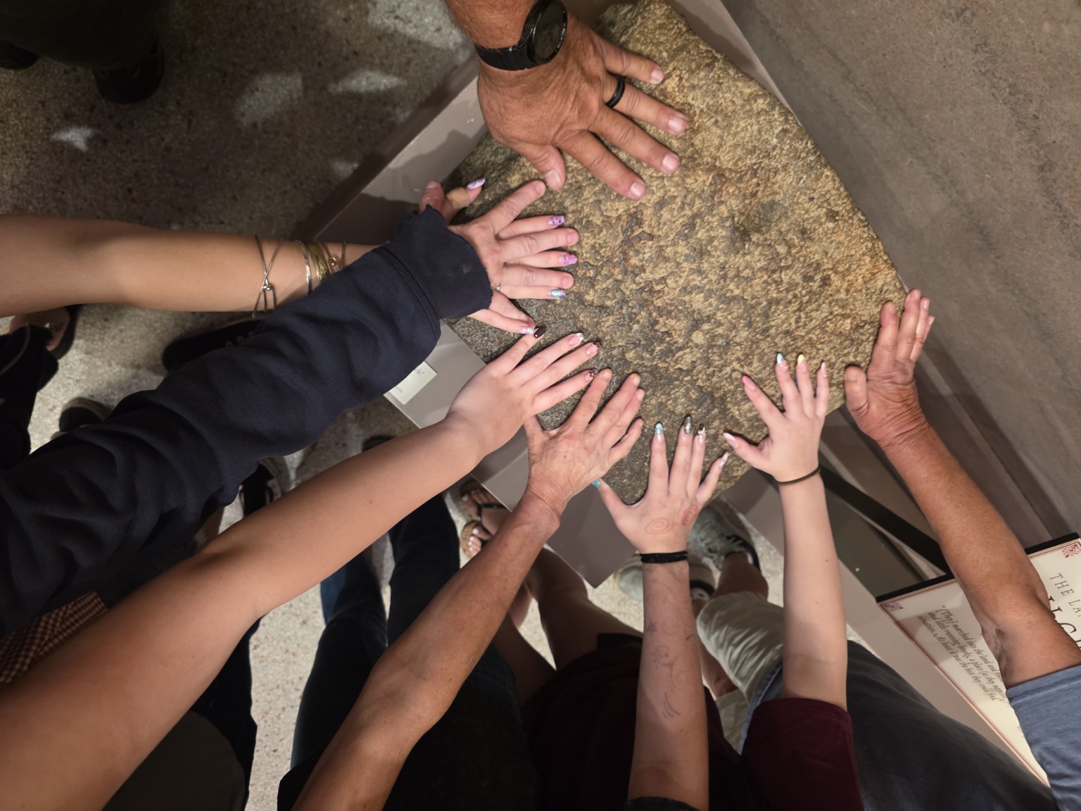 The Trail Tater crew placing their hands together on an authentic fragment of Plymouth Rock at Pilgrim Hall Museum