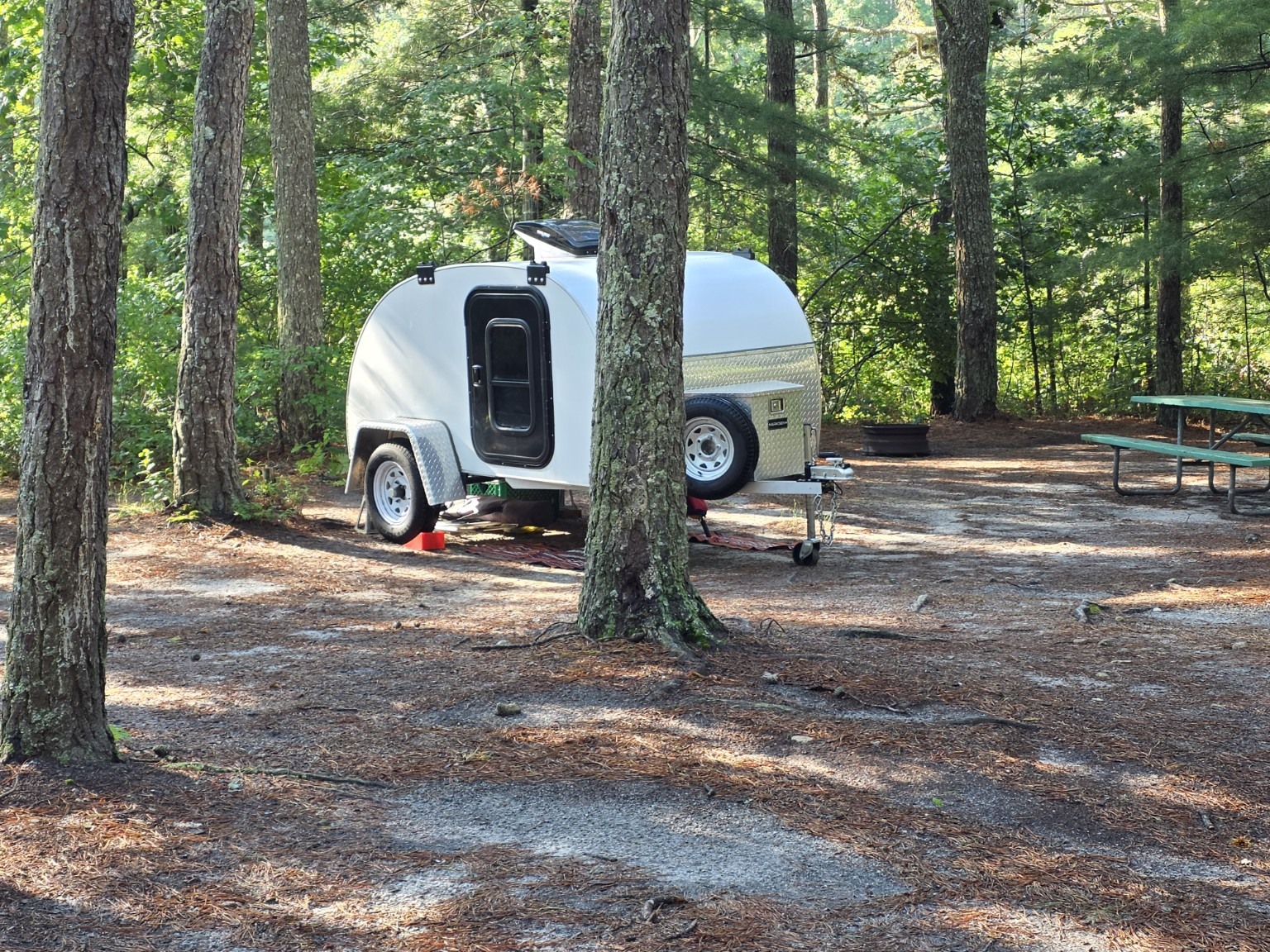 Small compact camper parked among the pine trees at Sandy Pond Campground