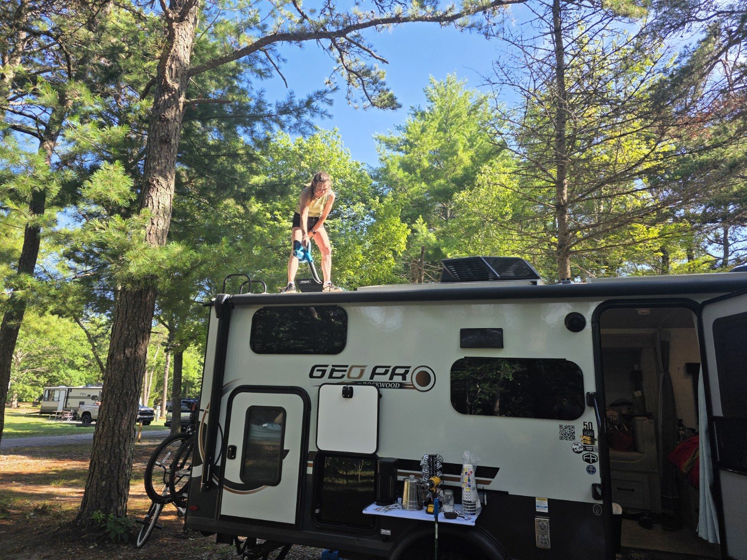 Lisa using a blower to clear the roof of Trail Tater while the crew breaks camp at Sandy Pond