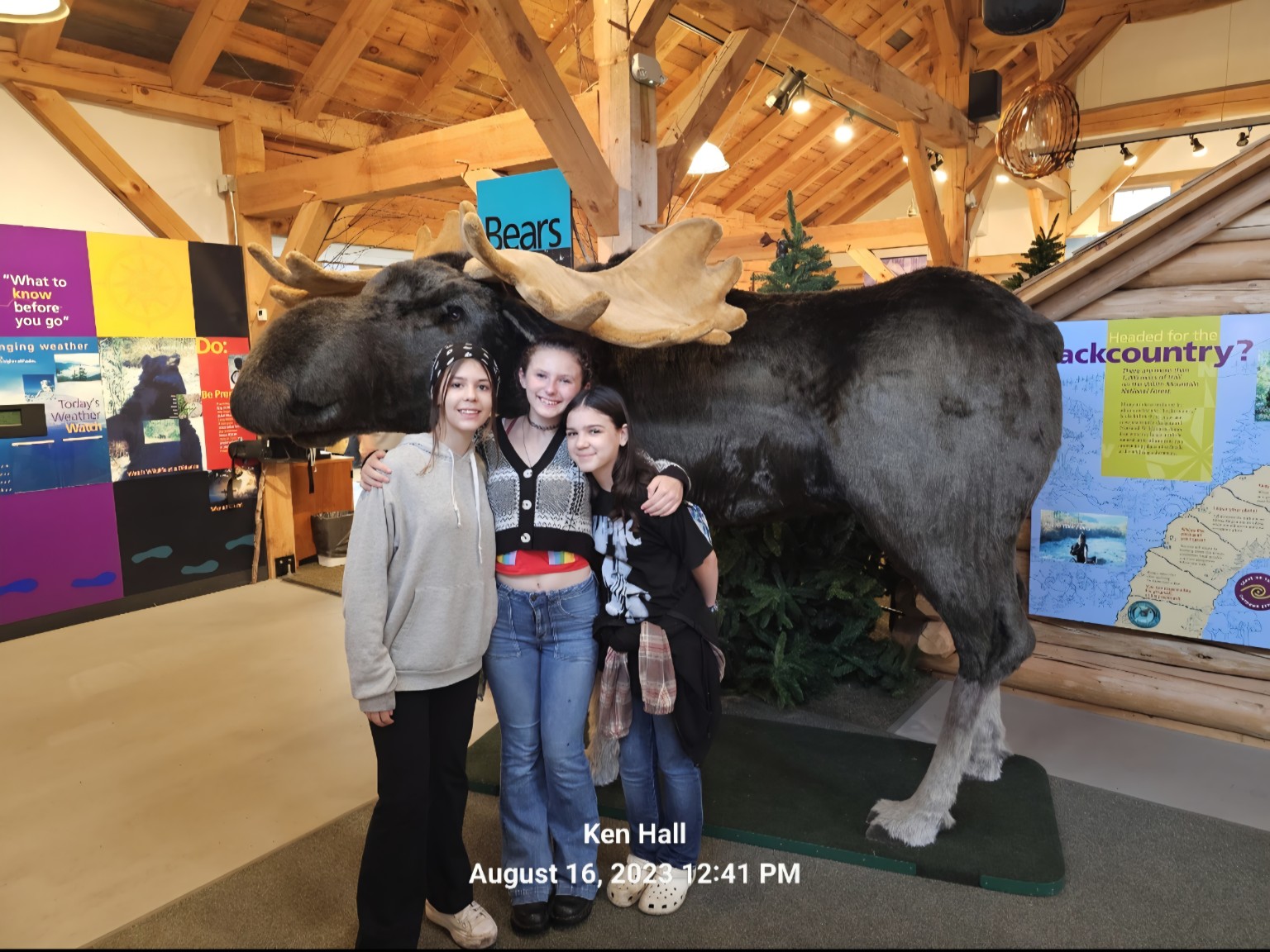 Three girls posing beside a large moose display at a White Mountains visitor center